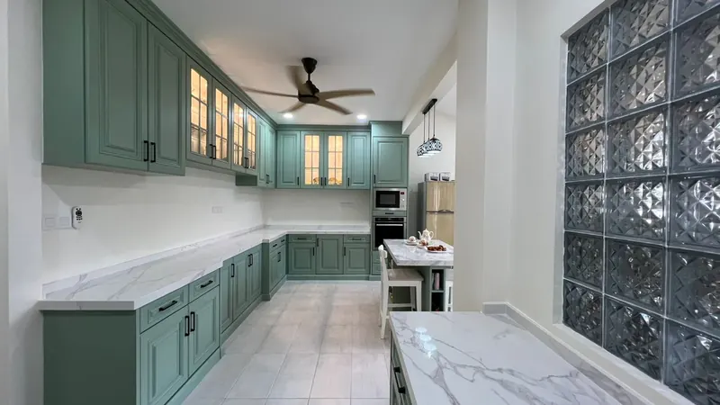 Completed L-shaped kitchen with sage green shaker cabinets, glass-front wall units and white marble worktops